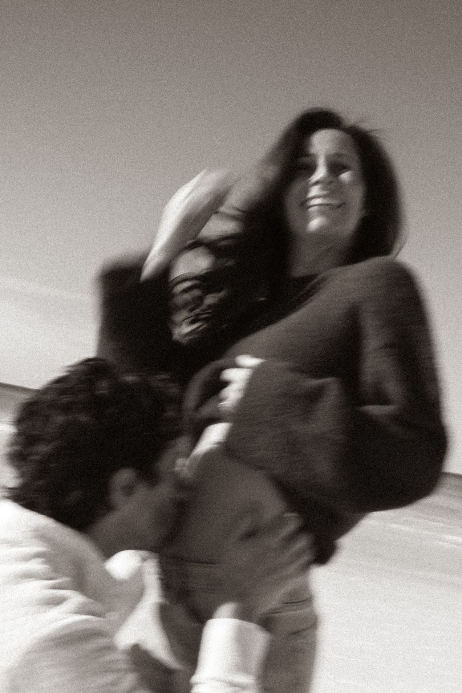 Black and white photo of a smiling woman being lifted by a man outdoors on a beach.