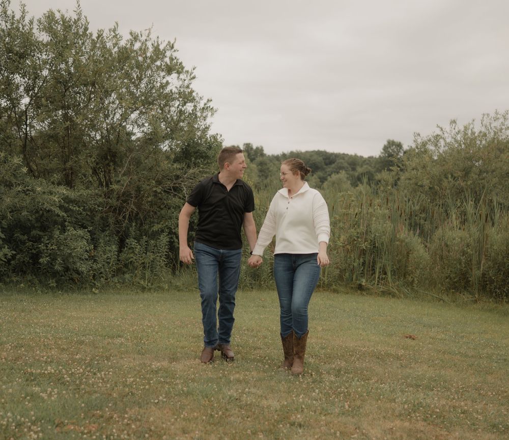Happy couple holding hands walking through green meadow on cloudy day.