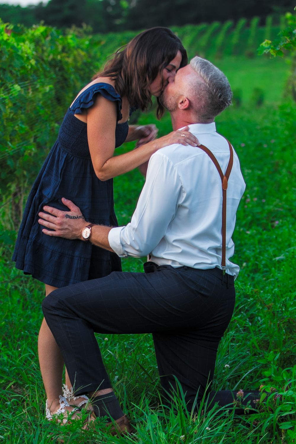 Romantic couple sharing intimate moments in a lush green vineyard setting wearing formal attire.