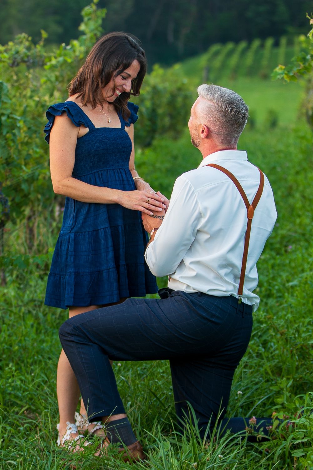 Couple poses together in a green field during an engagement photoshoot at sunset.