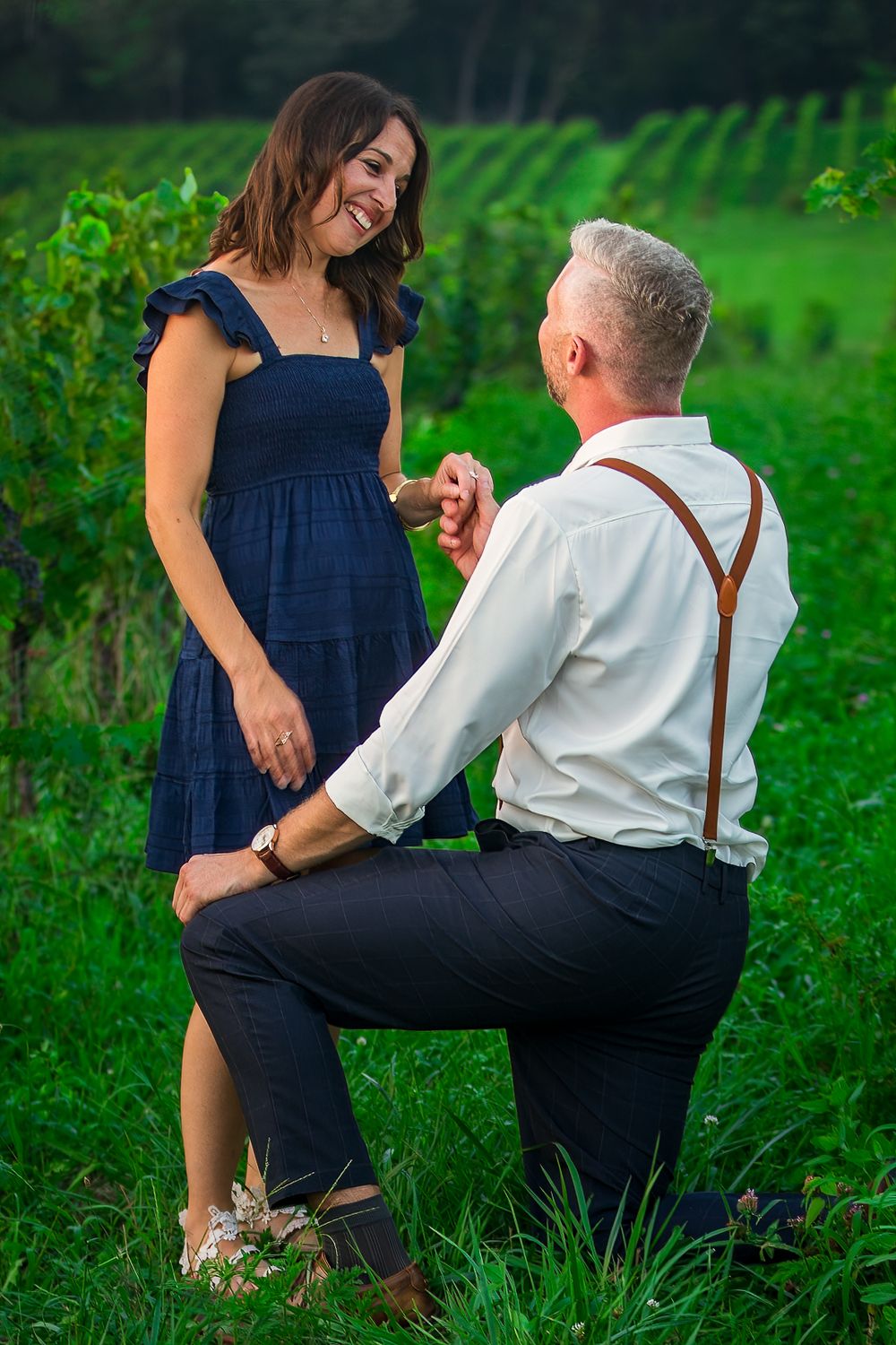 Couple in a romantic outdoor setting with navy dress and suspenders enjoying a tender moment in lush green field.
