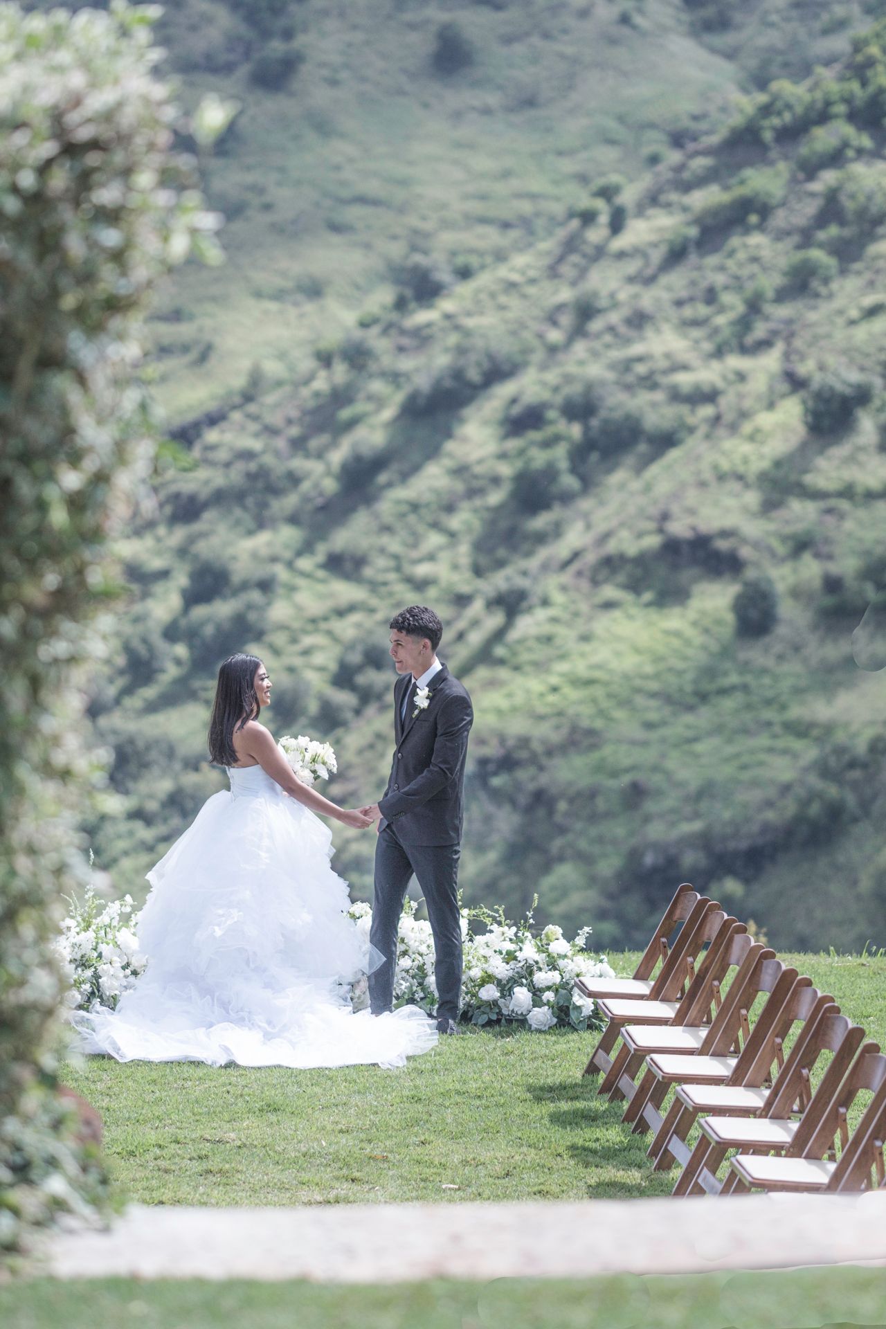 Bride and groom standing at an outdoor wedding ceremony site overlooking lush Hawaiian mountains.