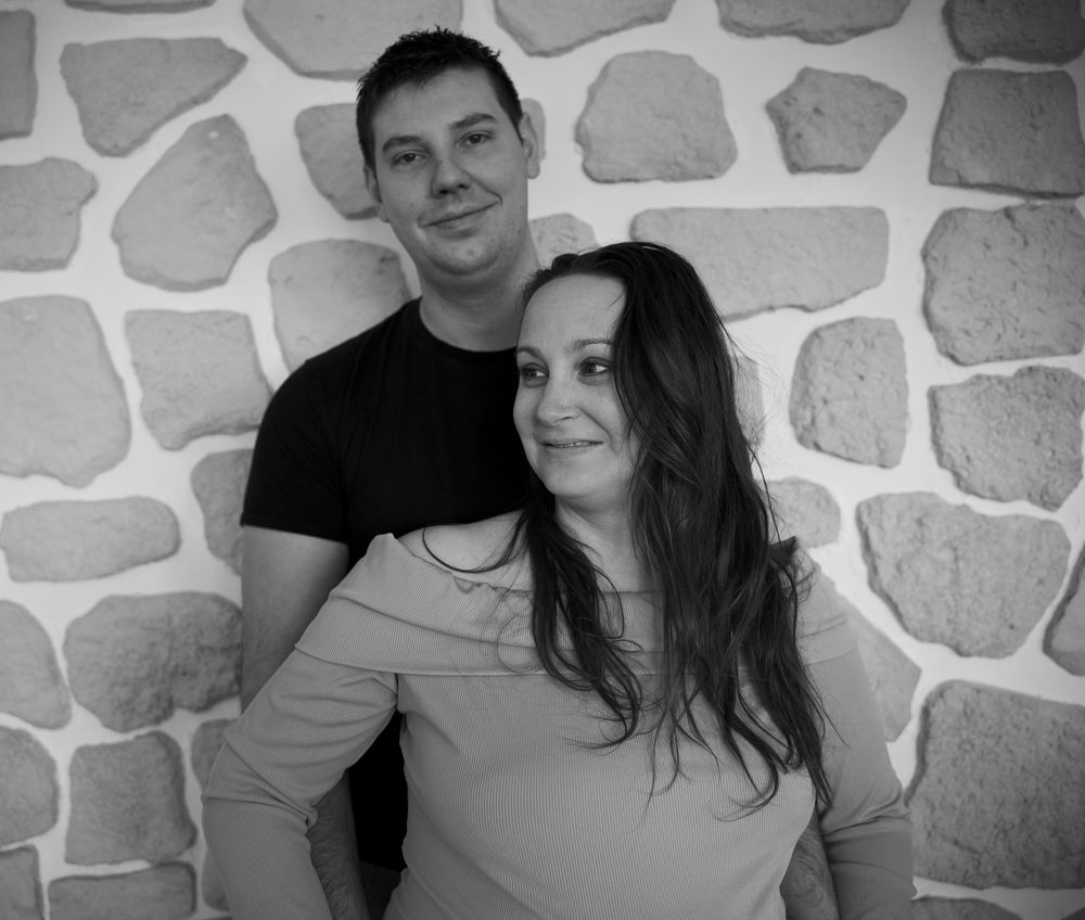 Couple en séance grossesse à Aix-en-Provence devant un mur en pierre, photo naturelle et complice des futurs parents.