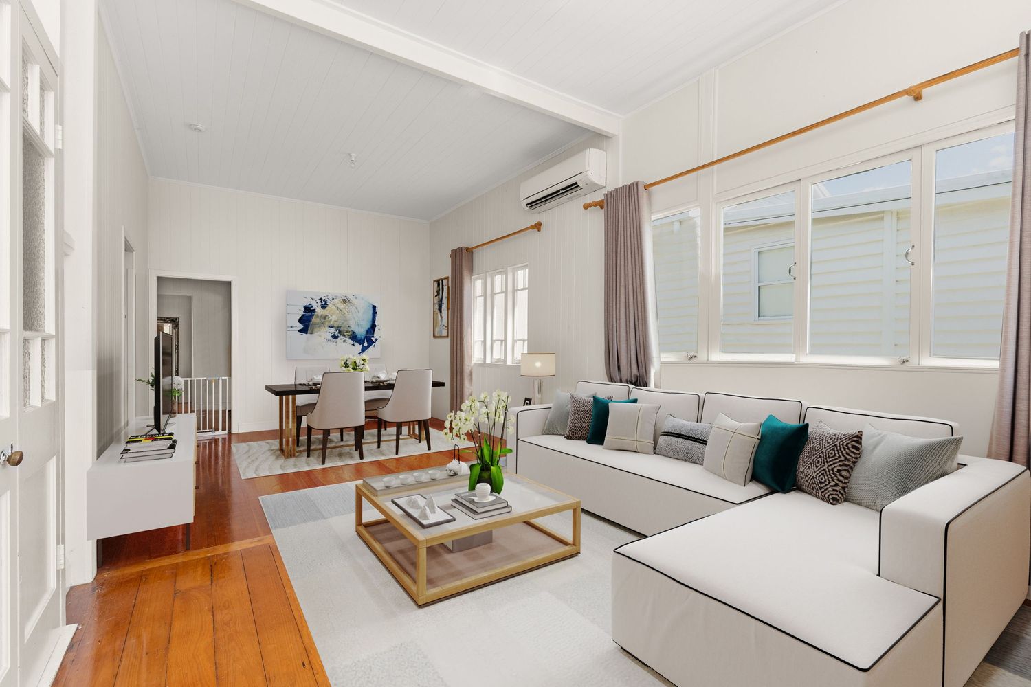 Spacious living and dining area with hardwood floors, white sectional sofa, split-system AC, and teal accents.