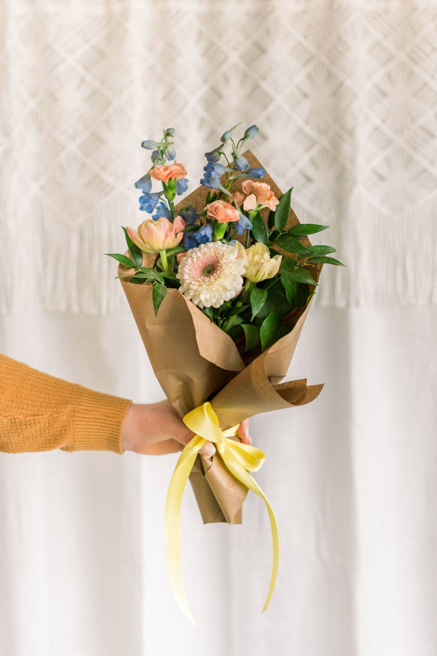 Brown paper gift bags with yellow ribbons hang in a row on a gray wall for an elegant party display.