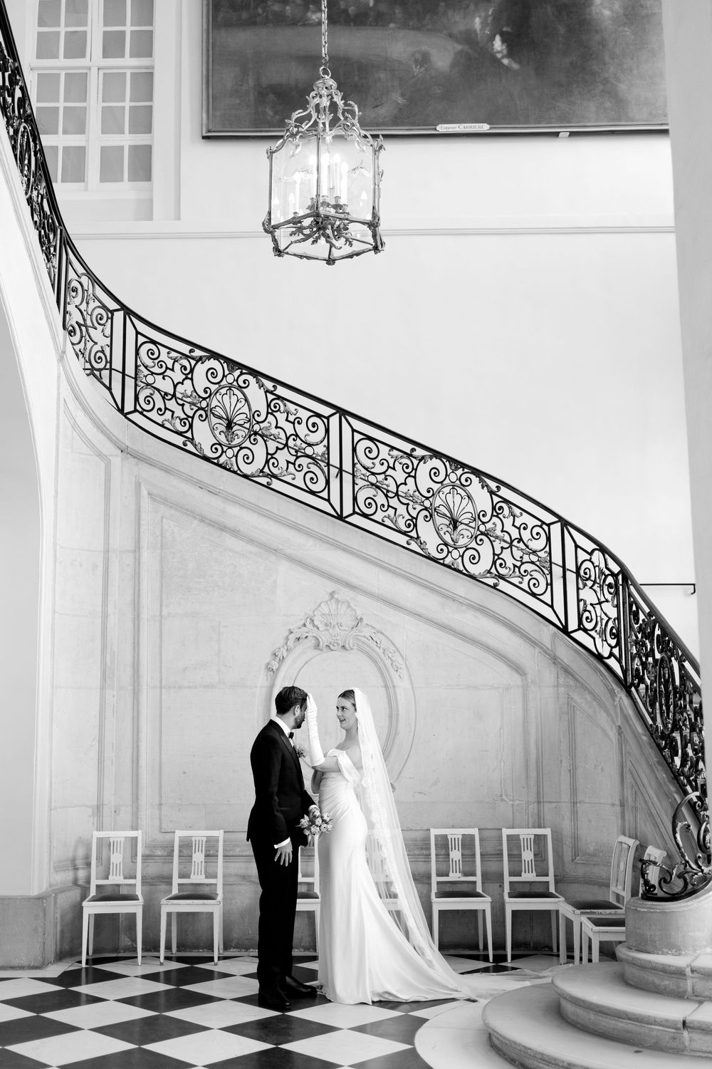 A black and white wedding photo series showing a couple on an elegant curved staircase with ornate iron railings.