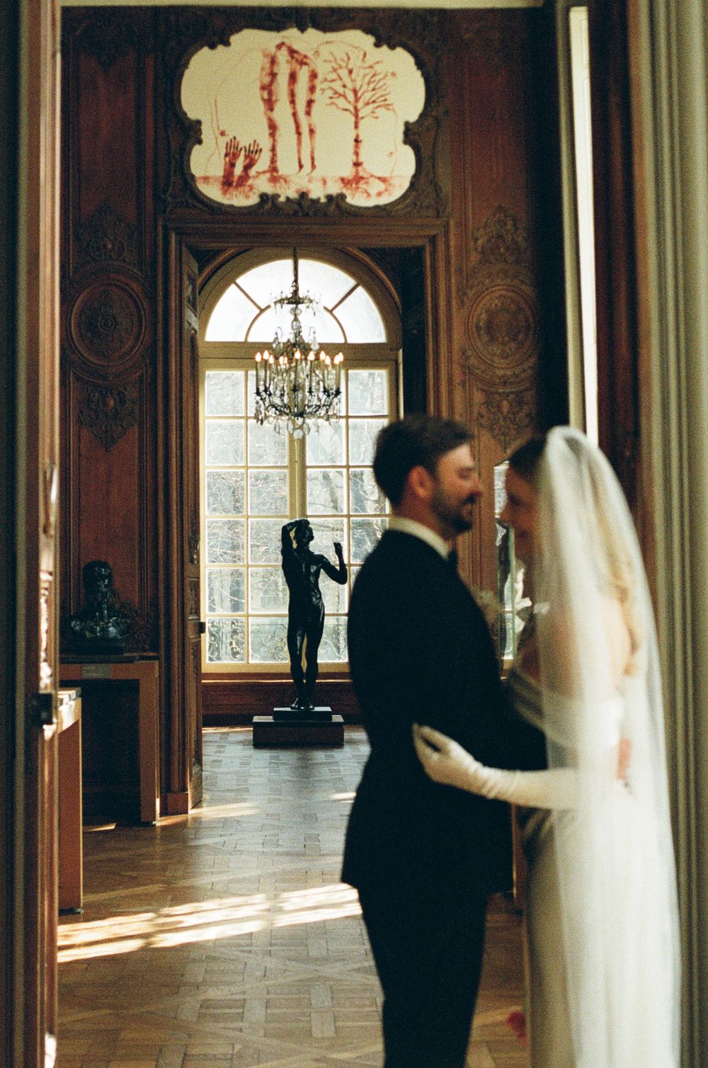 People in formal attire interact with tall white fabric installations in an elegant historic room with ornate walls and windows.