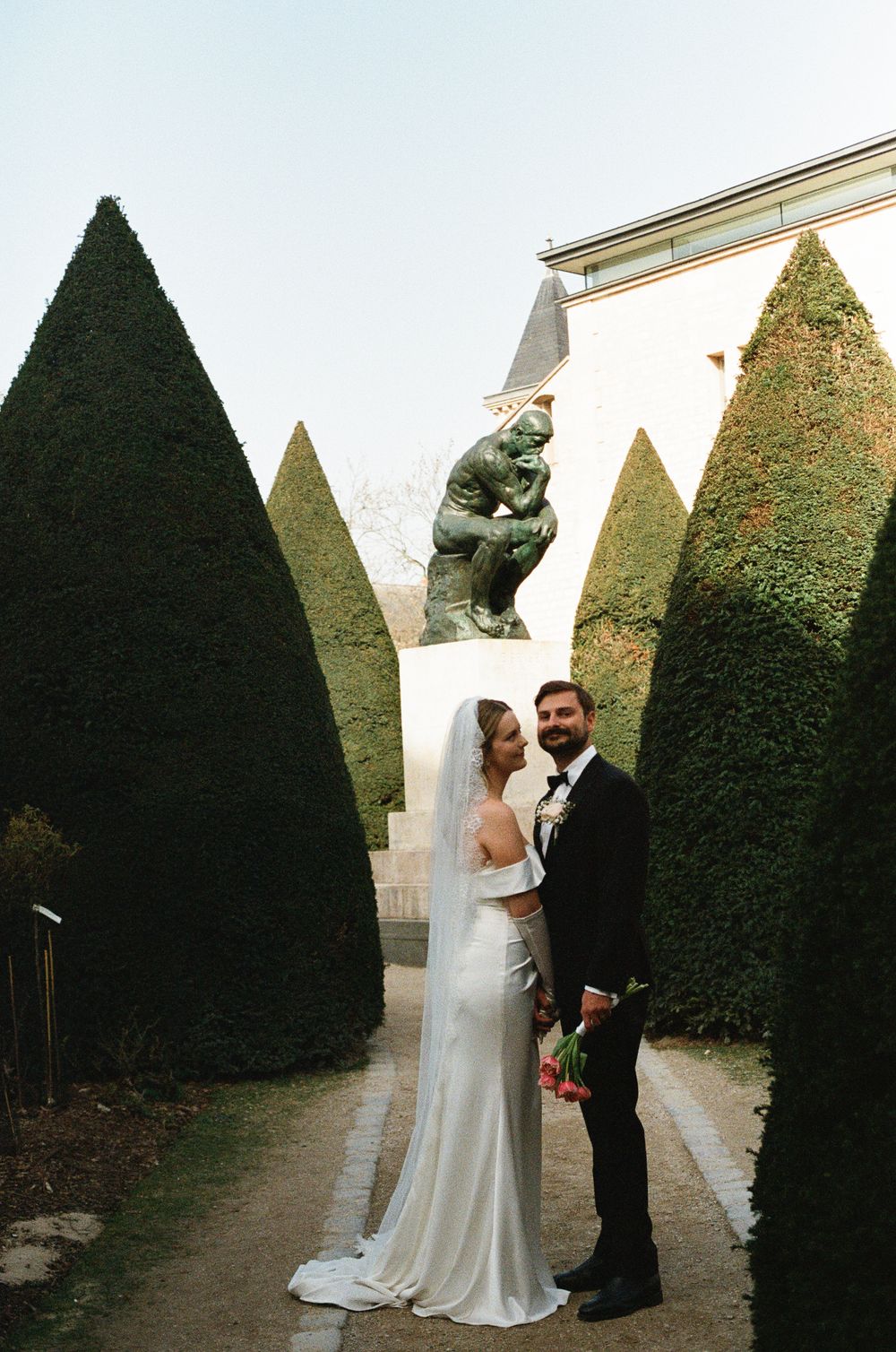 A couple shares romantic moments among tall manicured hedges in a formal garden setting during their wedding.