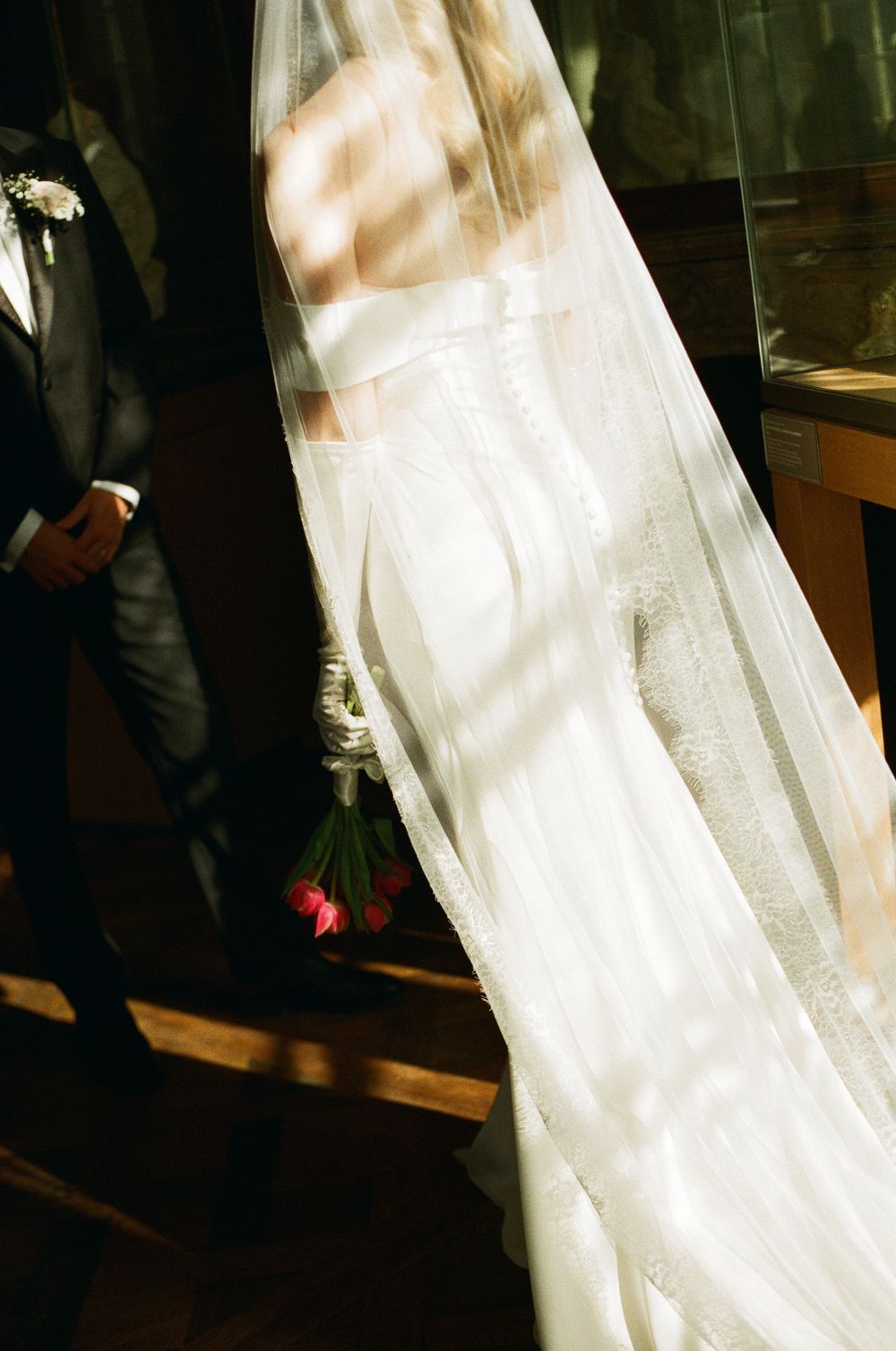 A flowing white wedding dress with delicate lace details hangs elegantly in dappled sunlight.