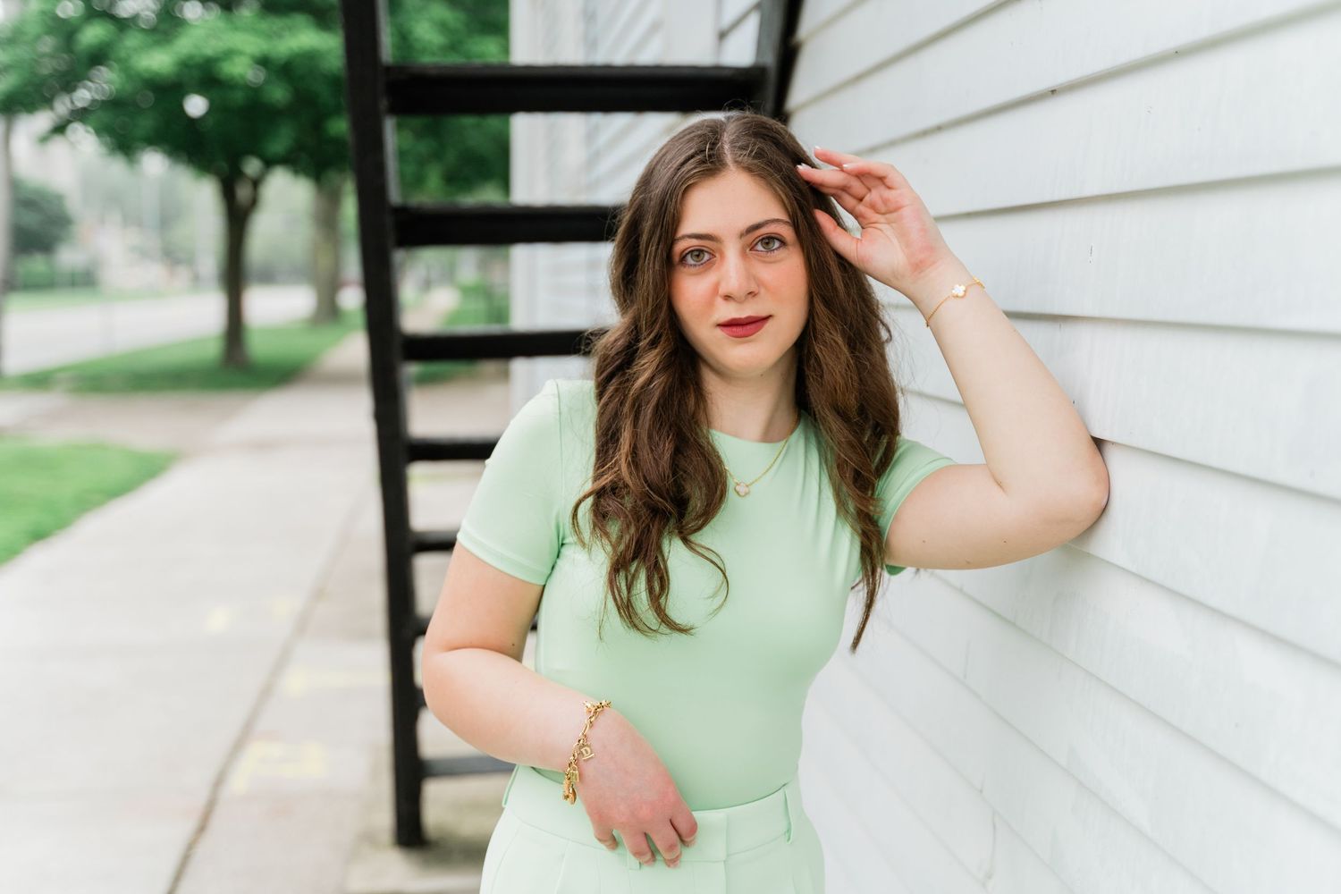 Toledo high school senior in mint green outfit poses against white wall in outdoor senior session in Downtown Perrysburg