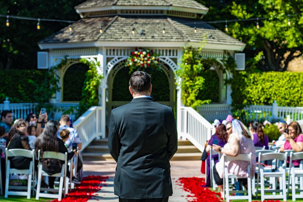 Elegant white gazebo decorated for outdoor wedding ceremony with red aisle runner and white chairs.