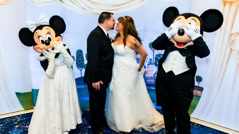 Bride and groom pose with Mickey and Minnie Mouse characters at a Disney themed wedding celebration.