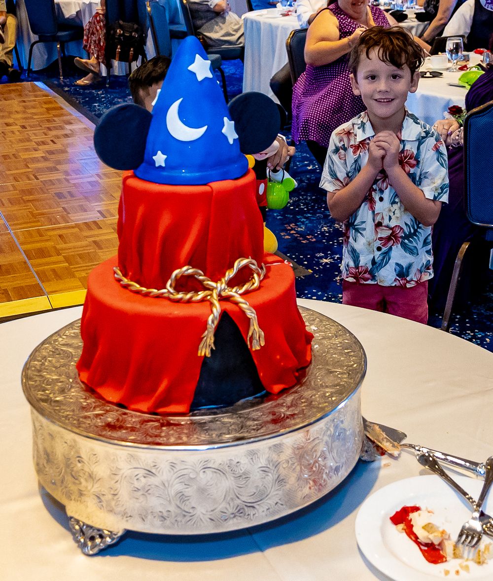 A blue and red Mickey Mouse-themed cake with stars and rope details sits on a silver platter during a celebration.