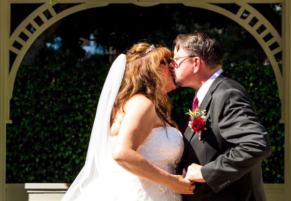 A romantic wedding couple shares a tender kiss under an elegant white gazebo during their outdoor ceremony.