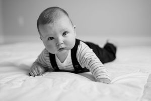 Black and white photo of an infant lying on white bedding while looking up at the camera.