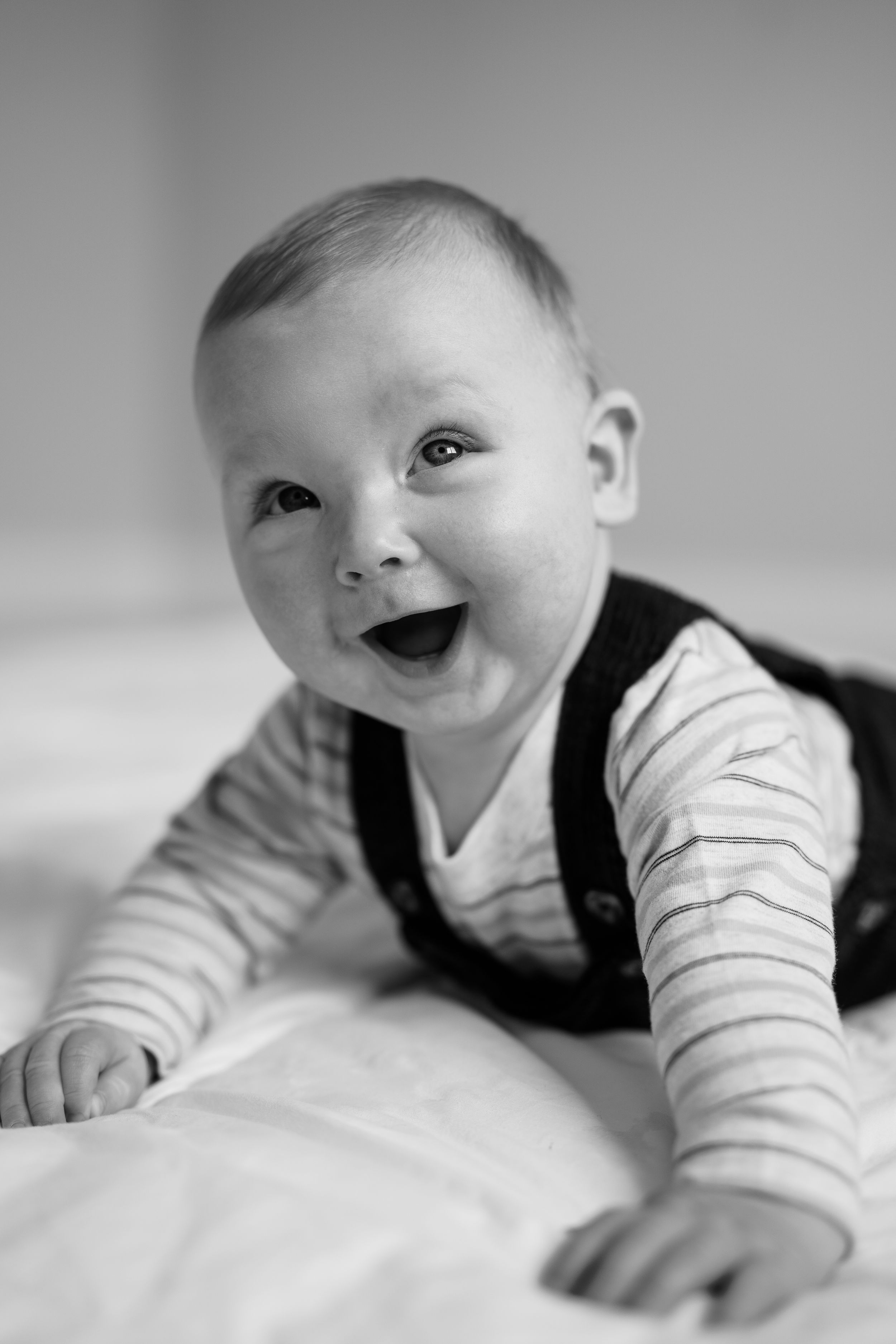 A series of black and white photos showing a baby lying on white bedding making playful expressions and movements.
