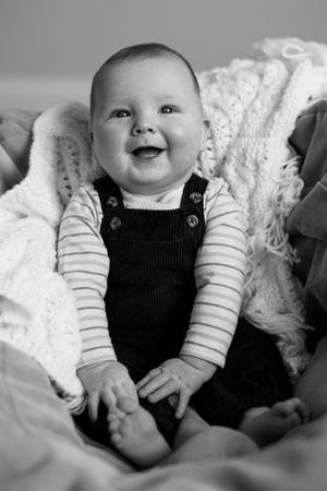 Sequence of black and white photos showing a happy baby in overalls on textured blankets.