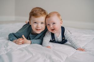 Two young children lying together on white bedding wearing coordinating outfits.