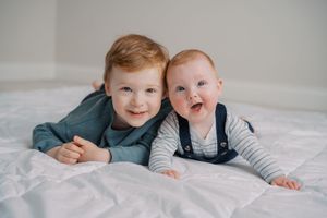 A collection of black and white photos showing children laying together on white bedding while smiling and laughing.