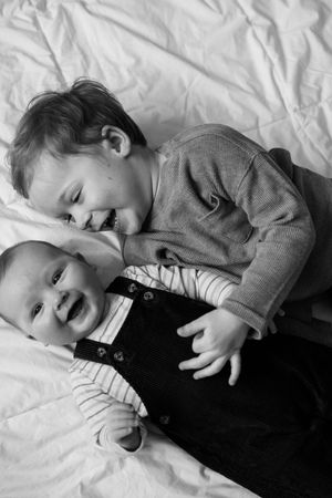 A black and white photo series shows a young child lying down and laughing on white bedding while wearing dark clothing.