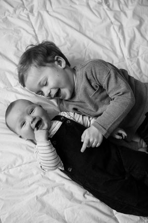 A series of black and white photos showing a young child in a gray sweater lying down and resting on white bedding.