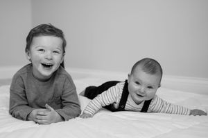 Black and white photo series capturing a baby in striped shirt and overalls showing various happy expressions.