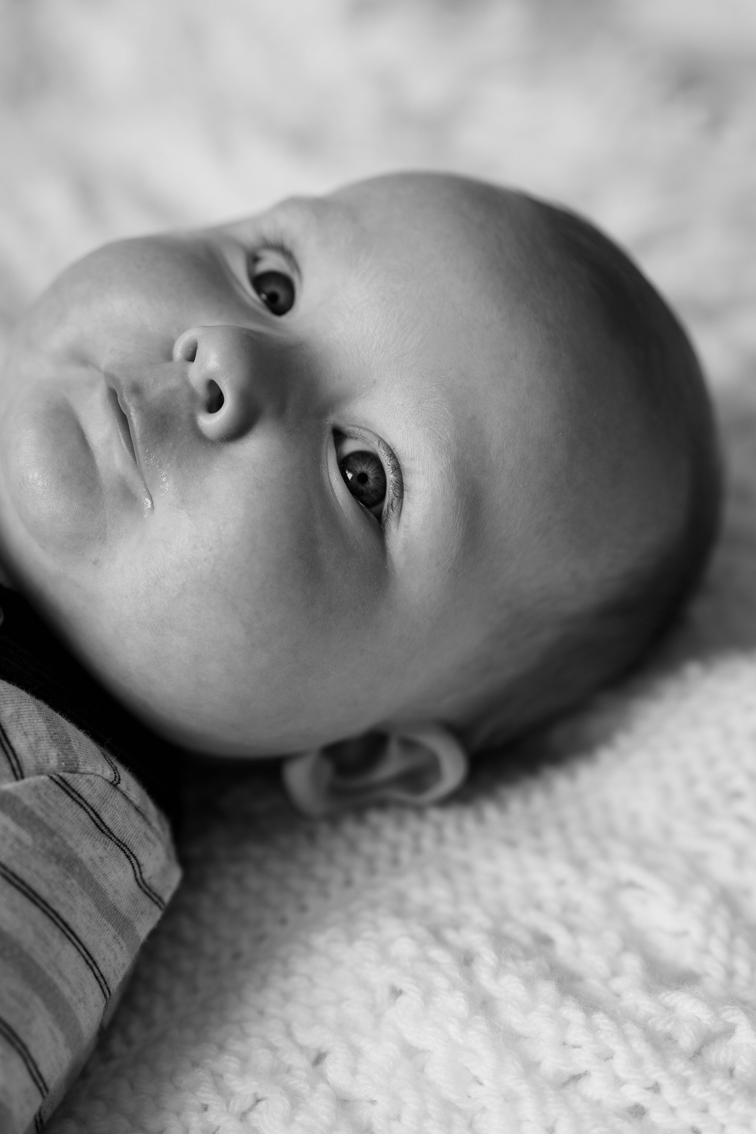A black and white photo series showing a baby lying on a textured surface from different angles.