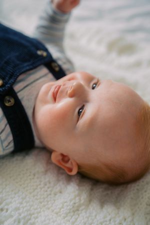 Close-up profile view of a baby lying on white knitted fabric wearing navy blue clothing.