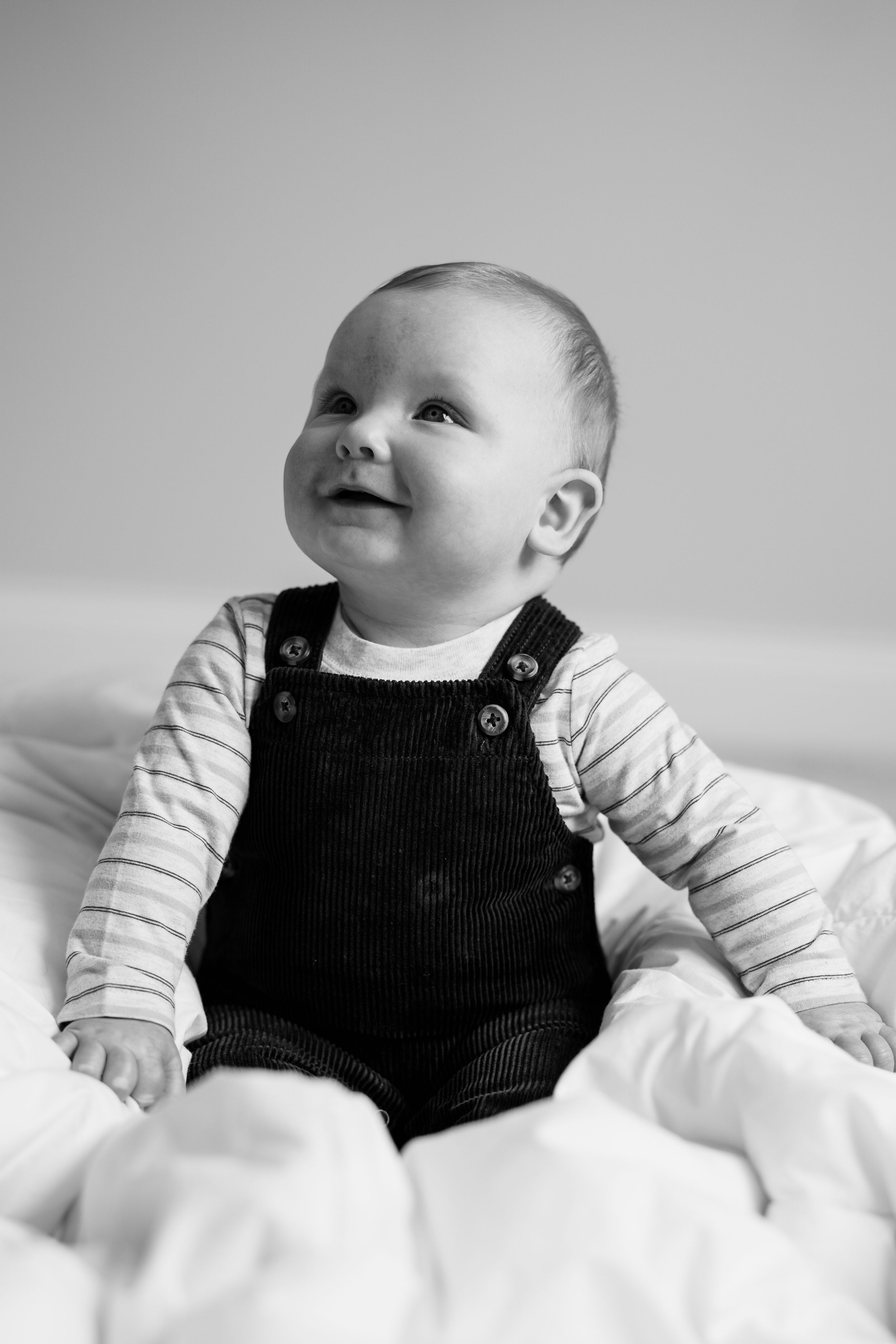 Black and white photo series of a baby in striped shirt and overalls lying on white bedding.