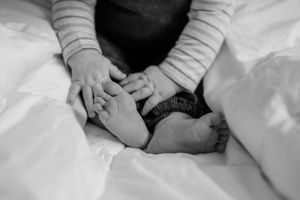 Close-up black and white shot of tiny baby feet and hands resting on white bedding.