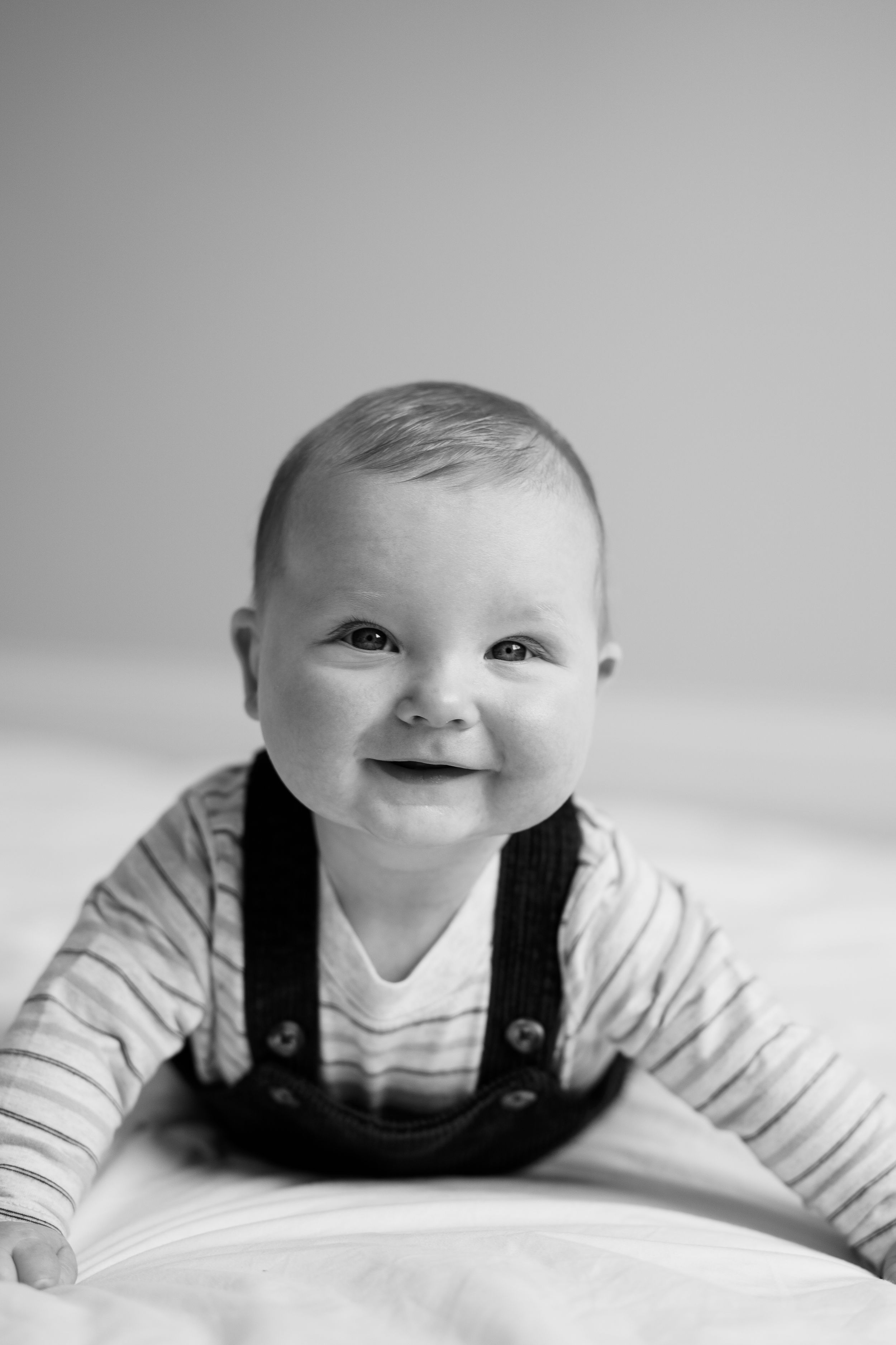 Black and white photo series showing a baby in overalls lying on their stomach with changing expressions.