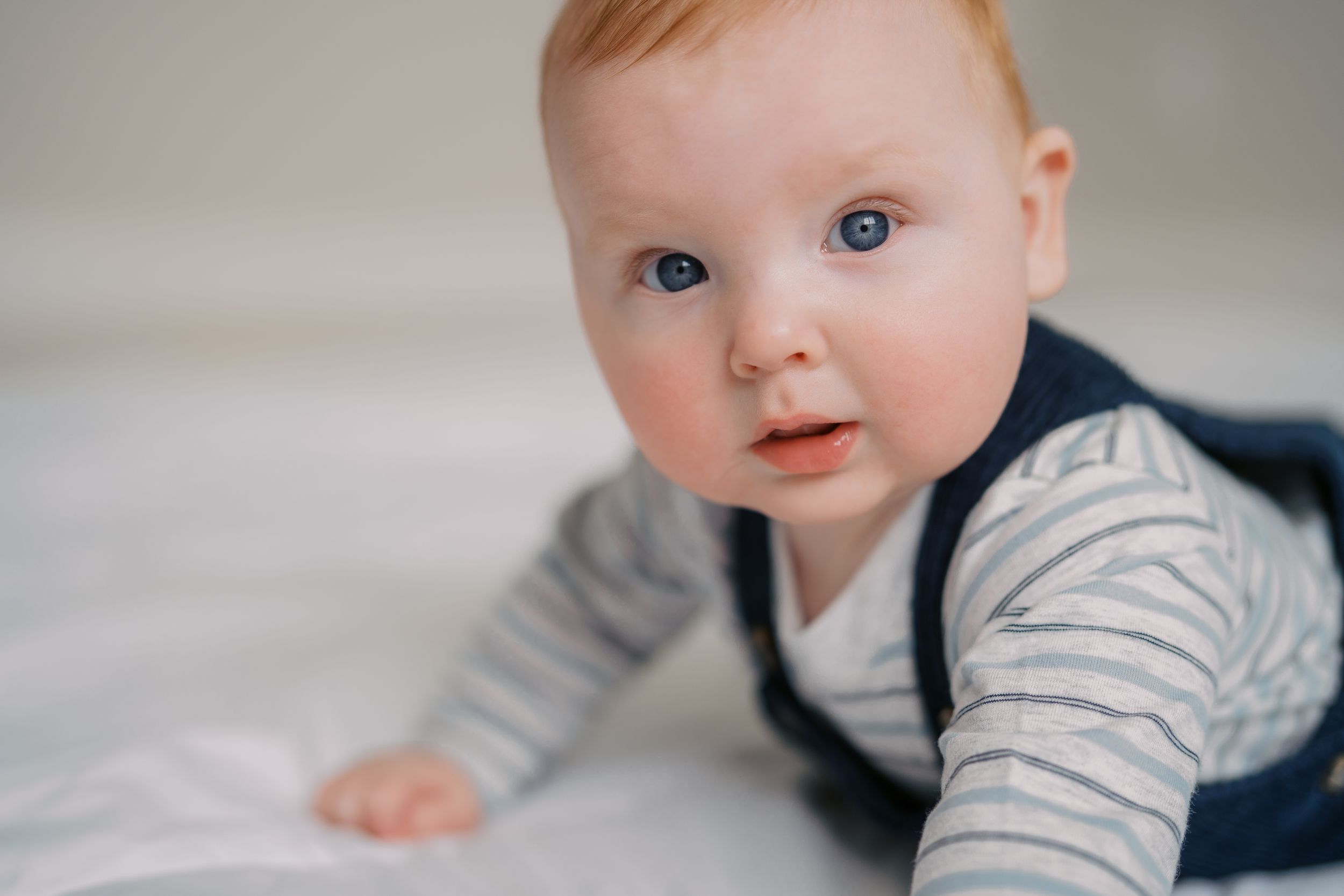 Baby in navy overalls and striped shirt showing playful expressions in a series of photos.