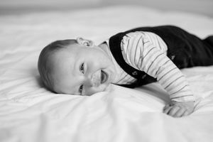 A series of black and white portraits showing a baby lying on white bedding in various poses.