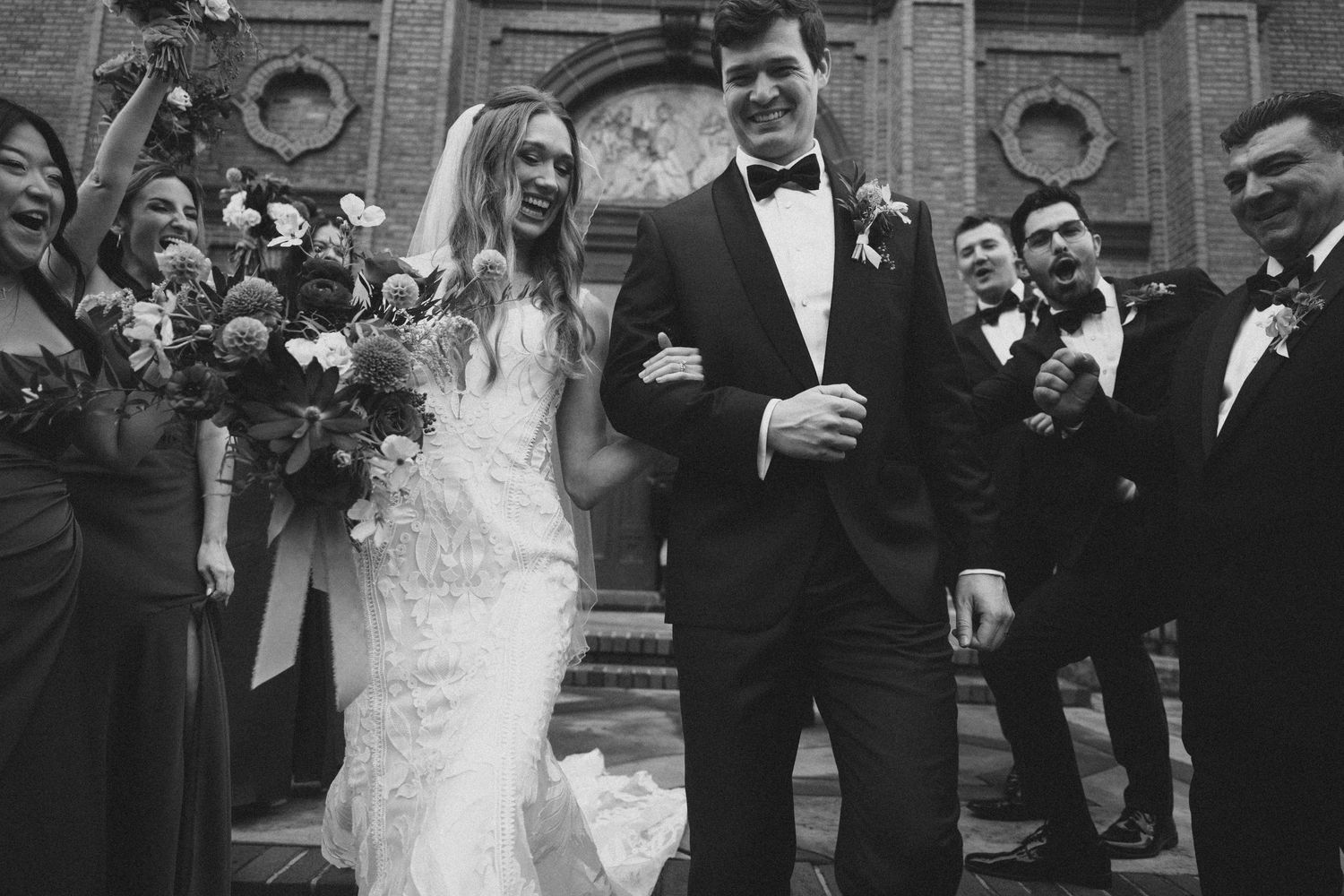 A black and white wedding photo showing a couple exiting a church while surrounded by joyful guests.