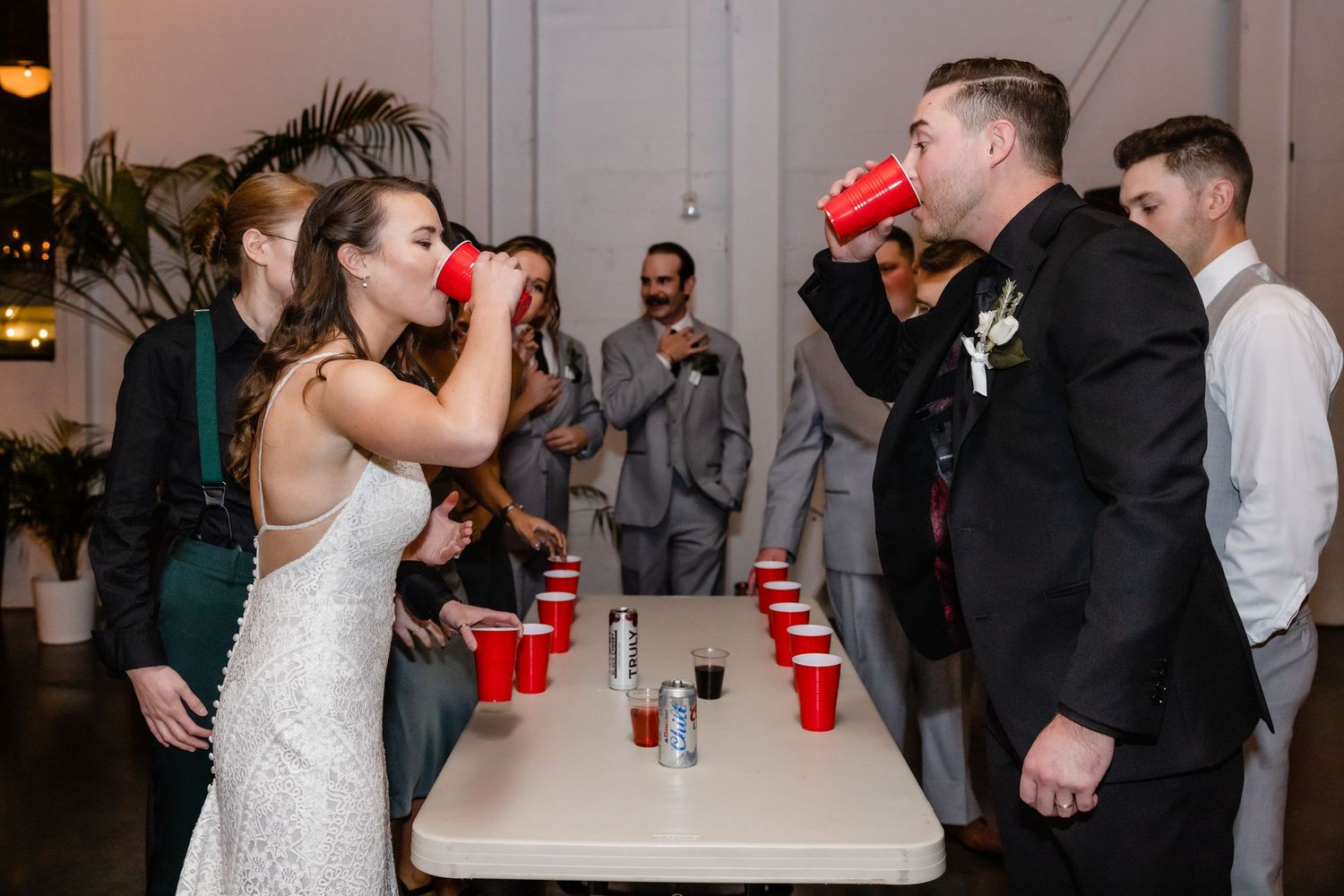 Wedding party guests dance and celebrate while drinking from red cups at an indoor reception.