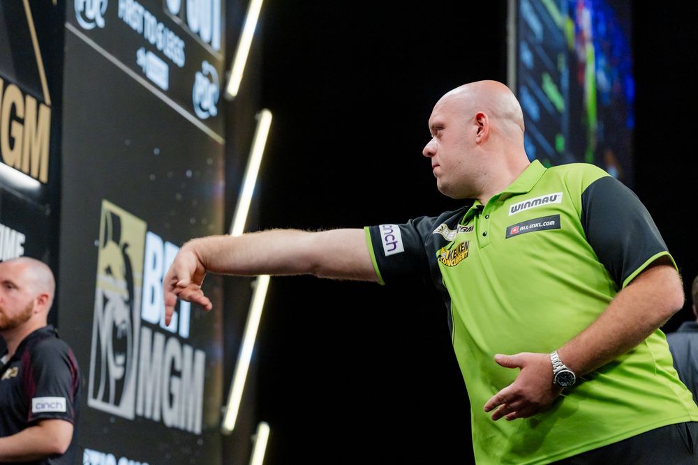 A man in a green shirt is playing darts on a stage in front of a crowd.