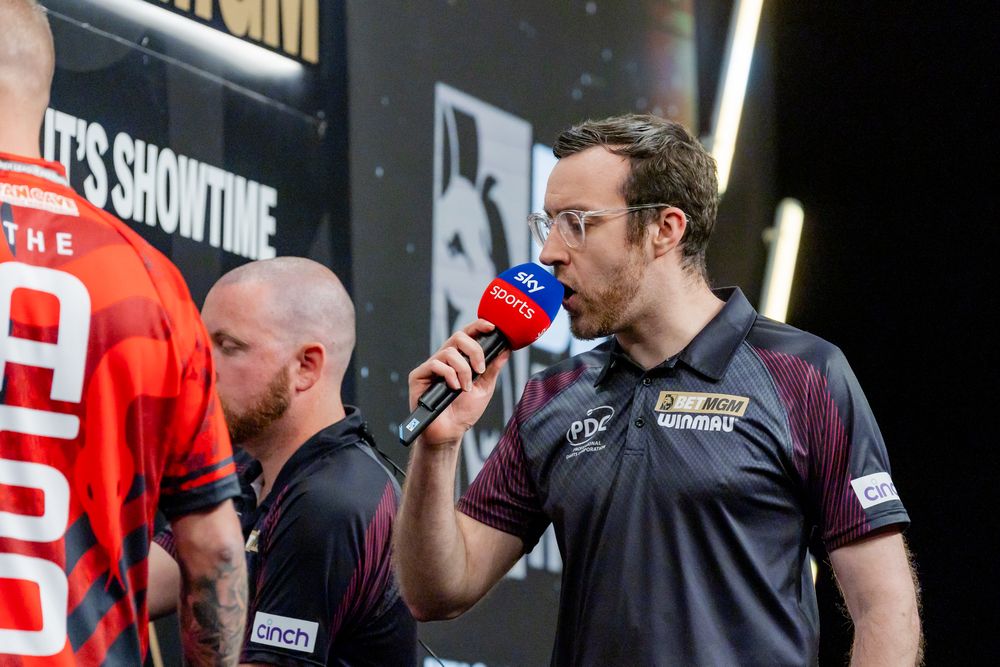 Two men speaking into microphones on a stage at an event.