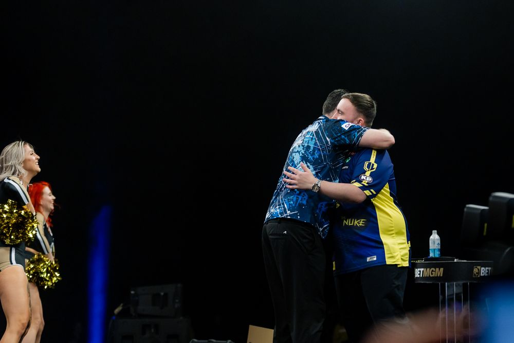 Two people in colorful outfits embrace on a stage in a performance setting.