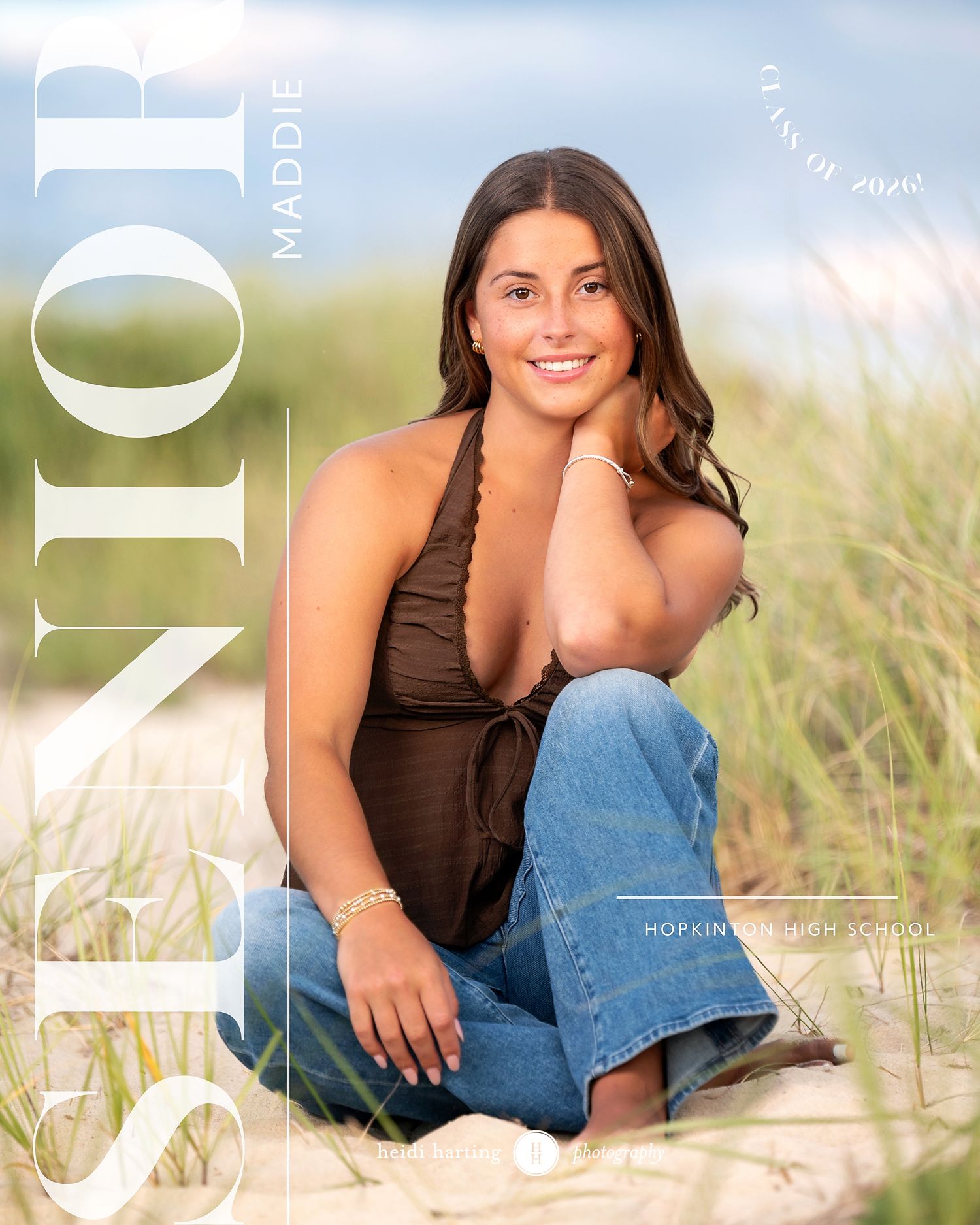 A person in a brown top and jeans sits casually on grass in an outdoor portrait setting.