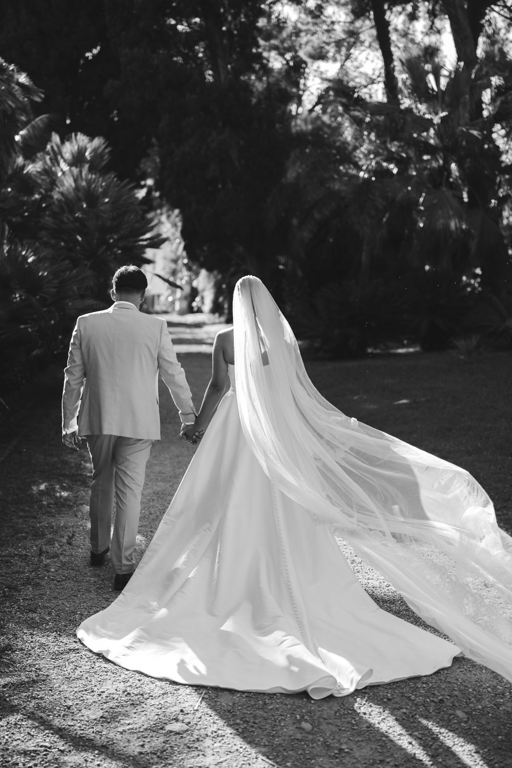 Bride wearing a long veil walking with her groom in the park of Villa Nobel in Sanremo.