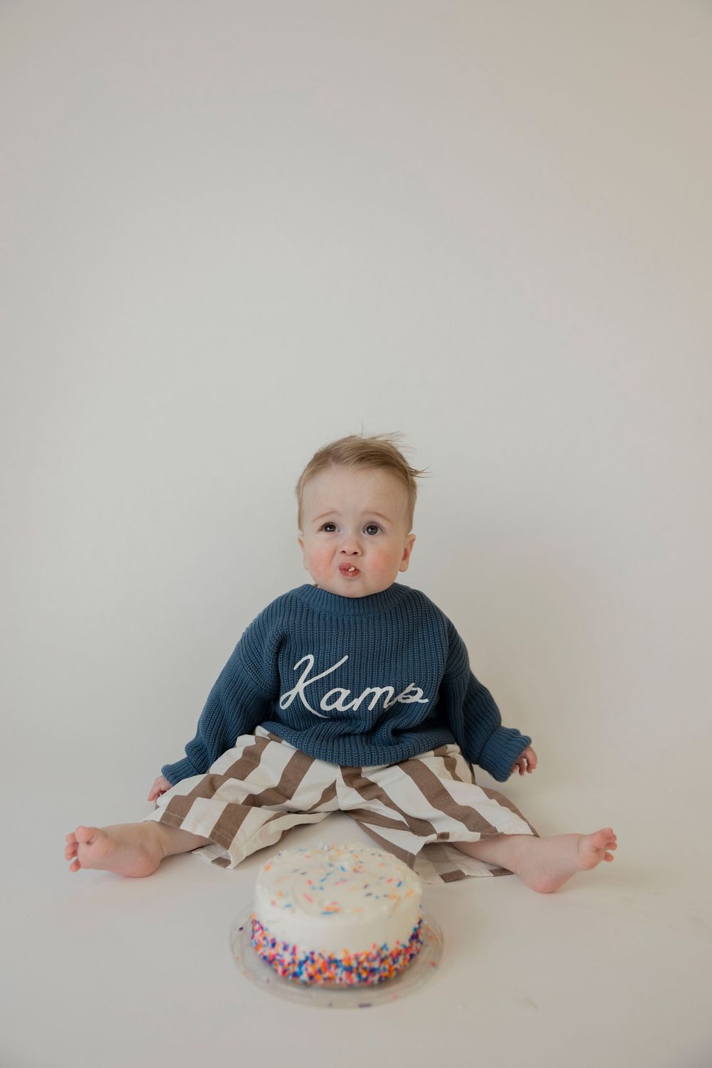 phot showing a baby in a navy sweater with a birthday cake on a white background in his Oxford michigan home