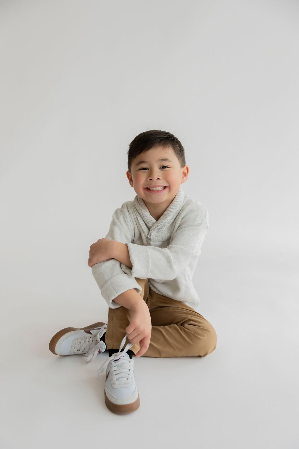 A child in a white shirt and khaki pants sits playfully on a white background showing various casual poses.