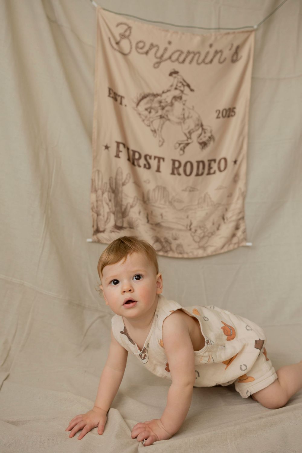 Baby boy crawling in front of Baby First Rodeo banner, wearing a cute western-themed romper.
