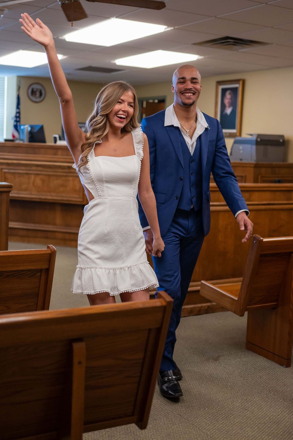 A couple in wedding attire walks joyfully through church pews in a candid moment.