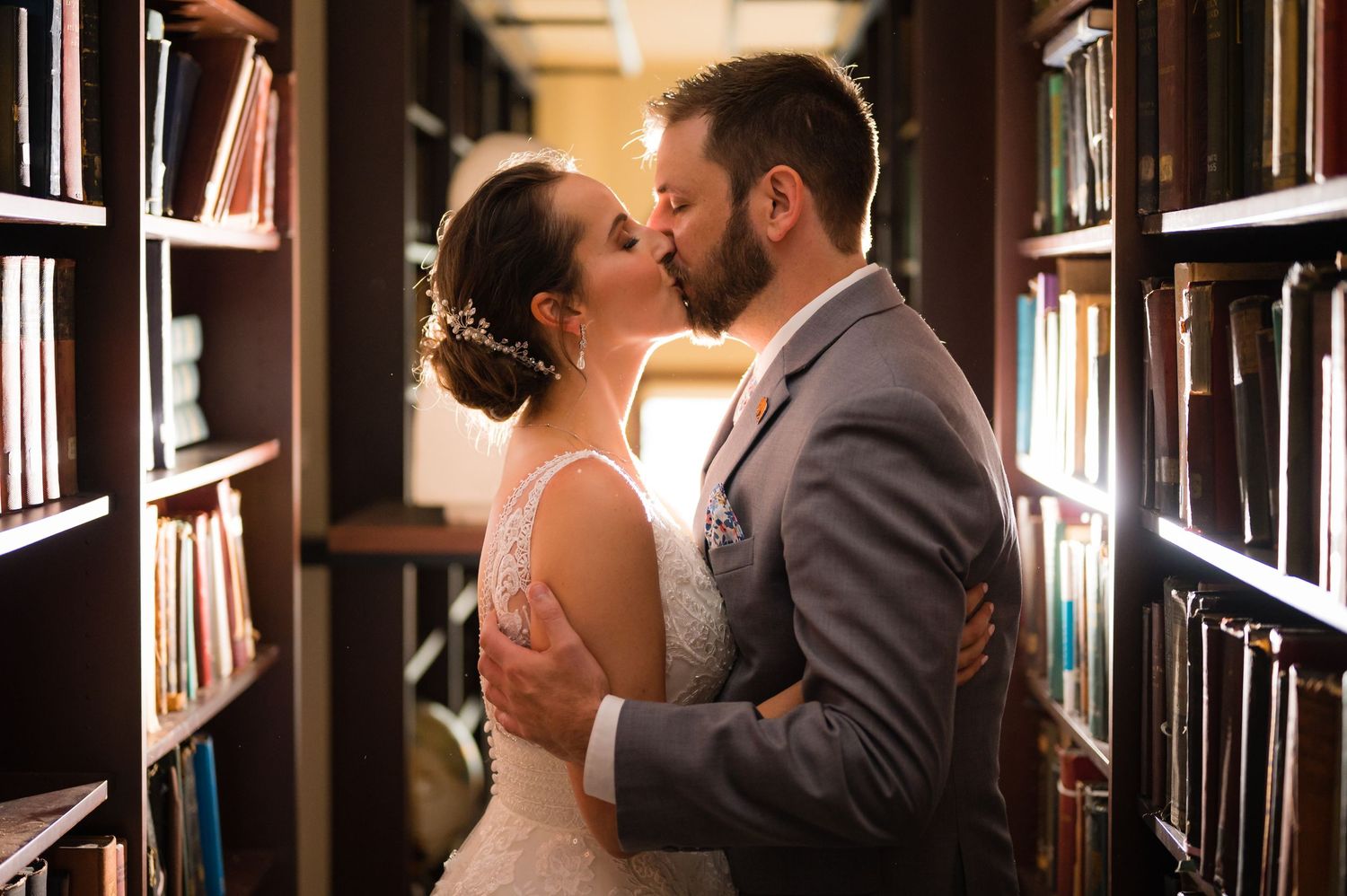 A couple shares an intimate moment in a cozy library setting with dark wood bookshelves and warm lighting.