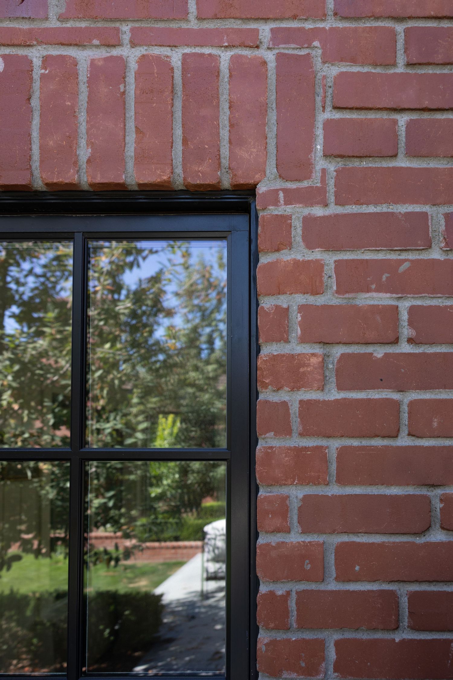 Exterior view of red brick wall with black-framed windows reflecting outdoor scenery and trees. Jen Wilbur Photos