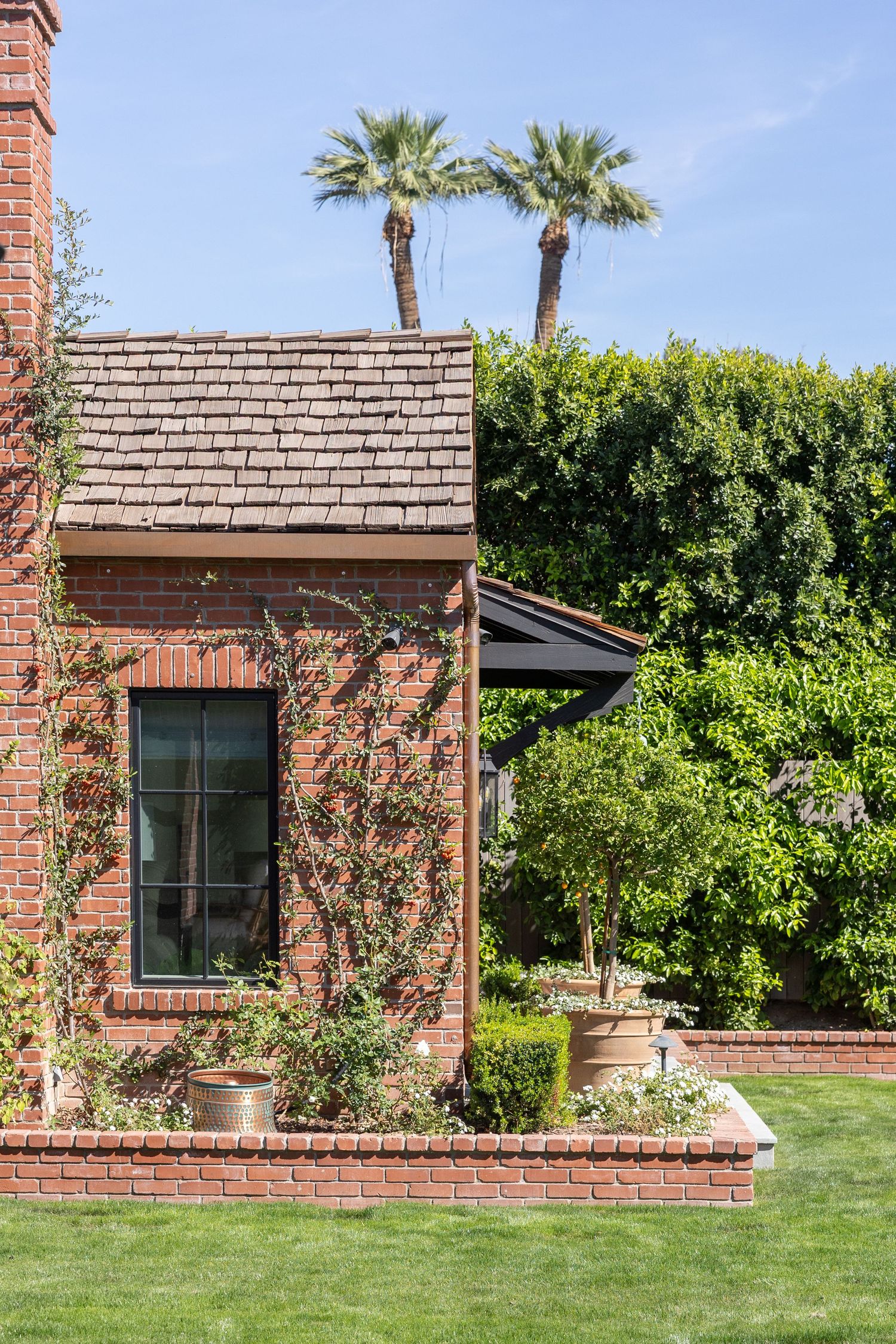 Exterior view of a brick house with green landscaping, palm trees and a shingled roof in a residential setting. Jen Wilbur Photos