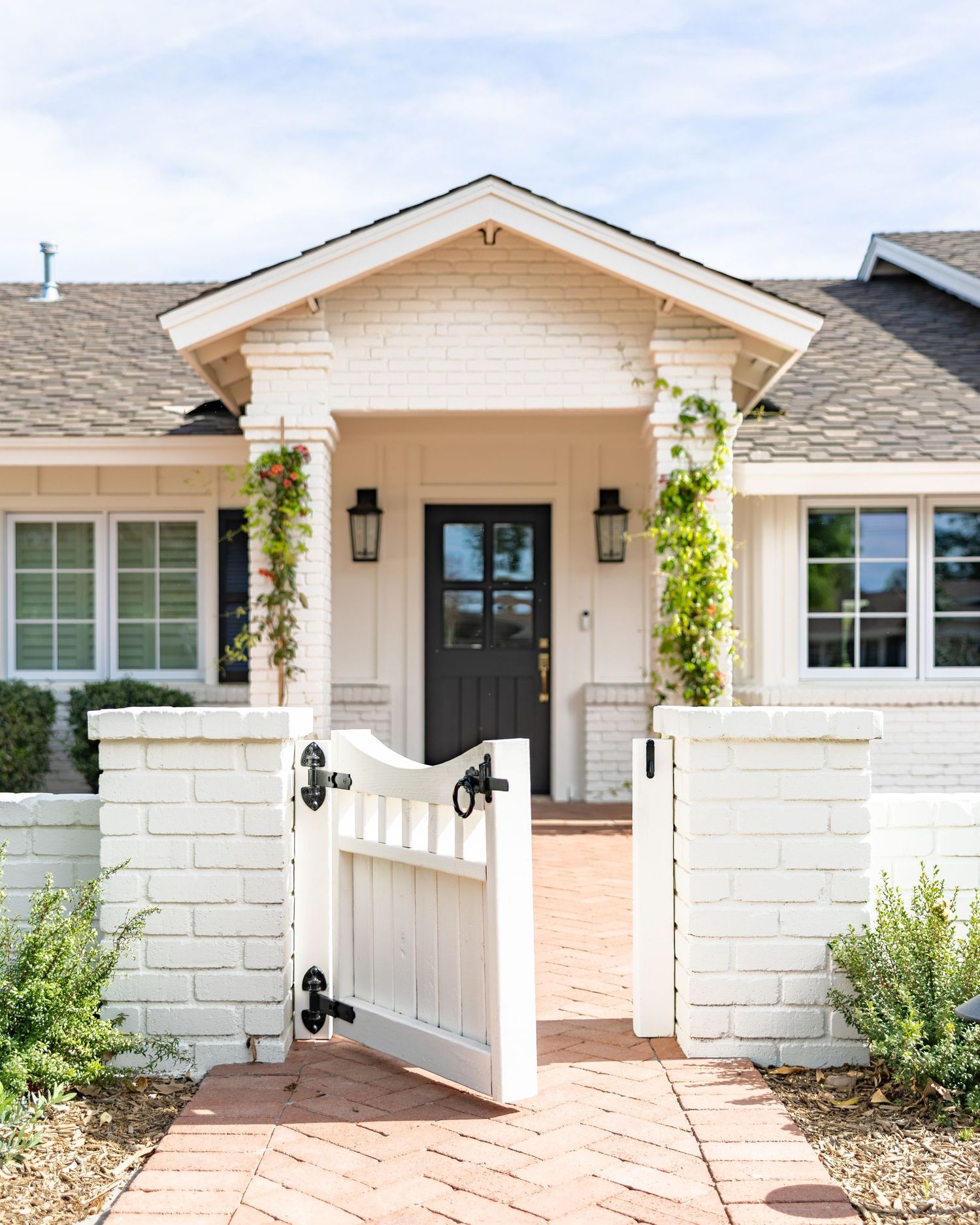 Exterior view of a modern ranch house with white brick walls, black shutters, and climbing vines around the entrance. Jen Wilbur Photos