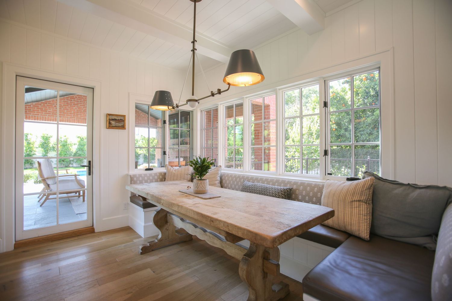 Modern dining area with built-in bench seating, pendant lights, and natural wood finishes in a bright sunlit space. Jen Wilbur Photos