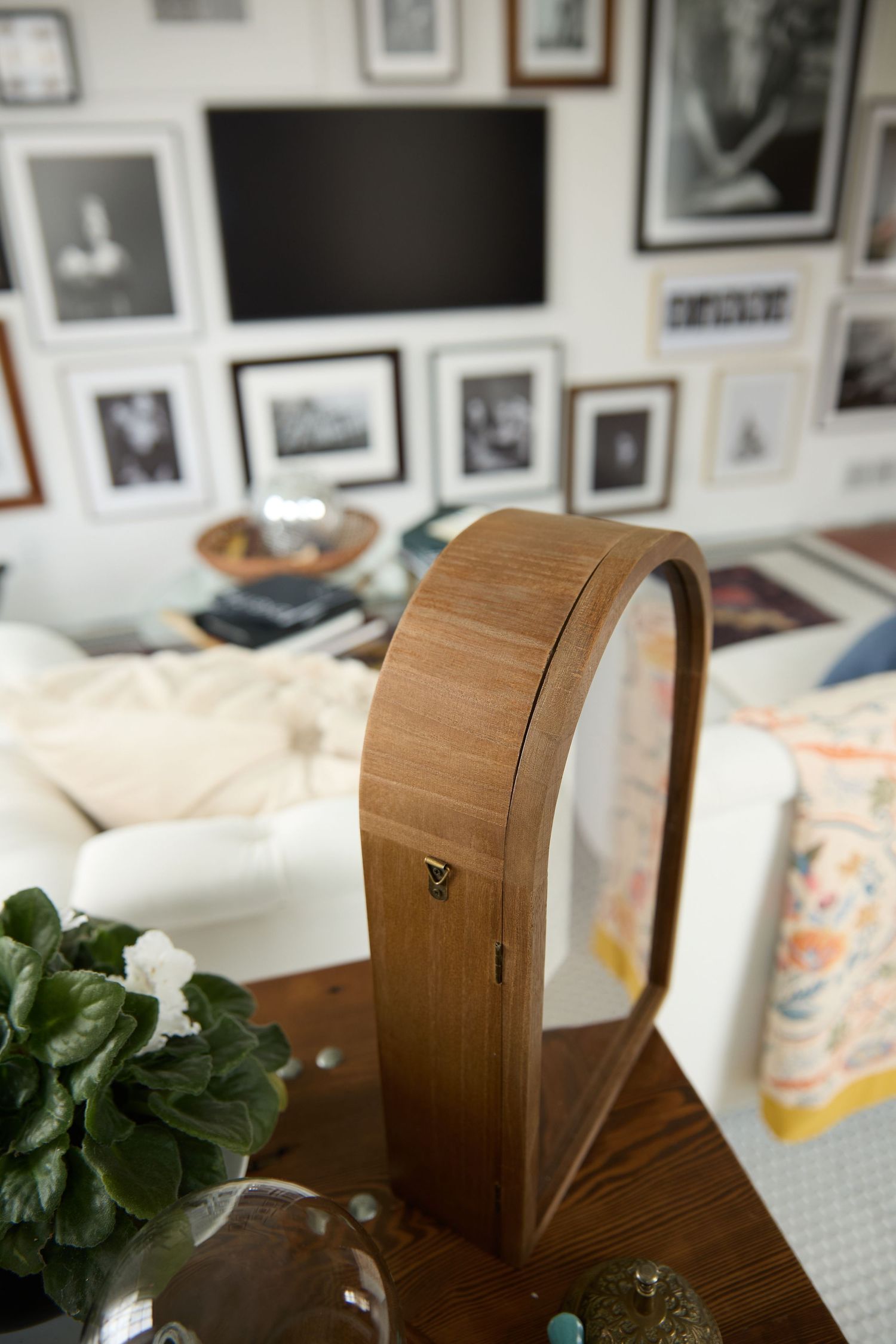 A curved wooden wall art piece with multiple panels stands against a white wall decorated with framed photographs.
